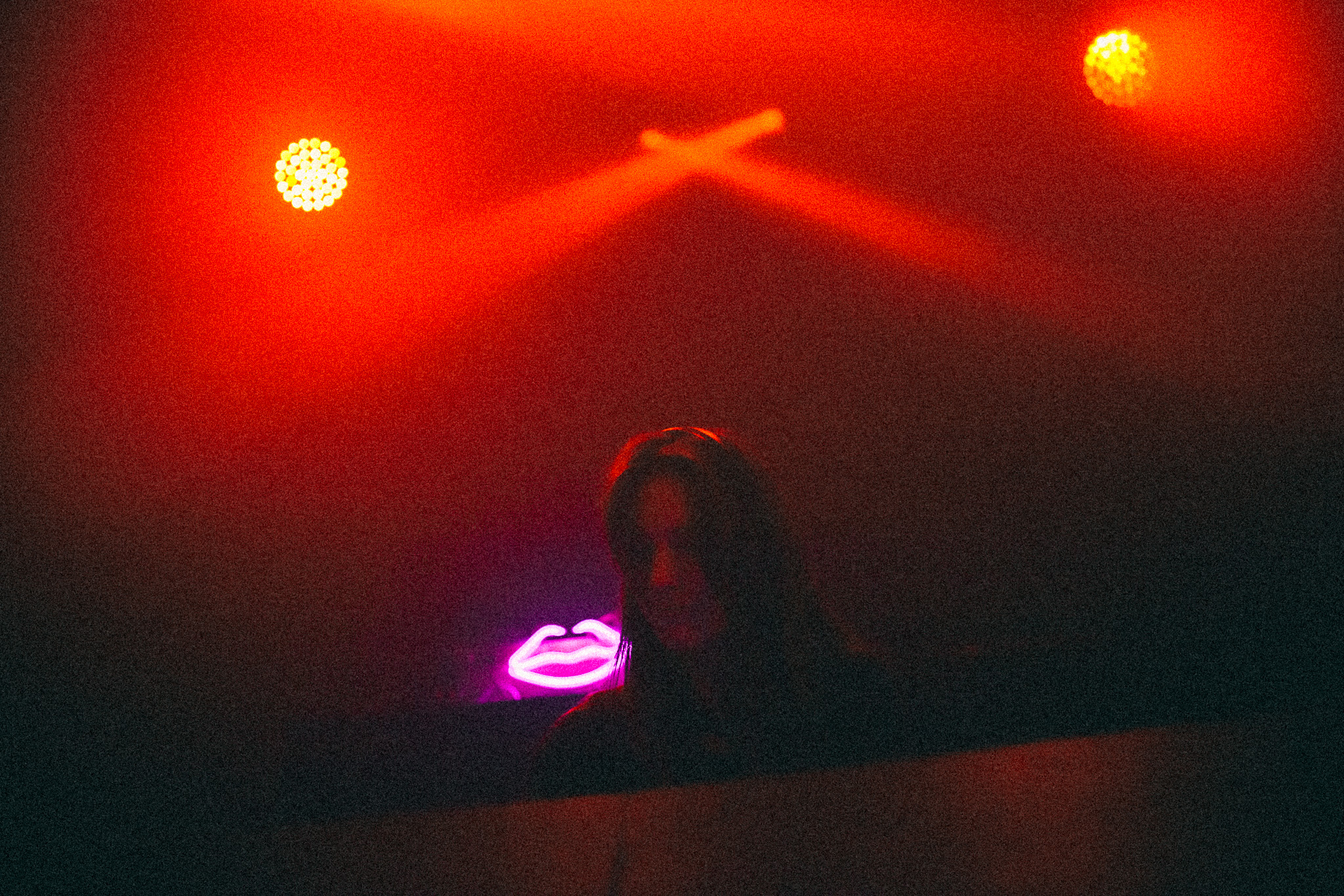 The room in deep red, two mirrorballs lit above, the booth small at the far end under a pink neon sign