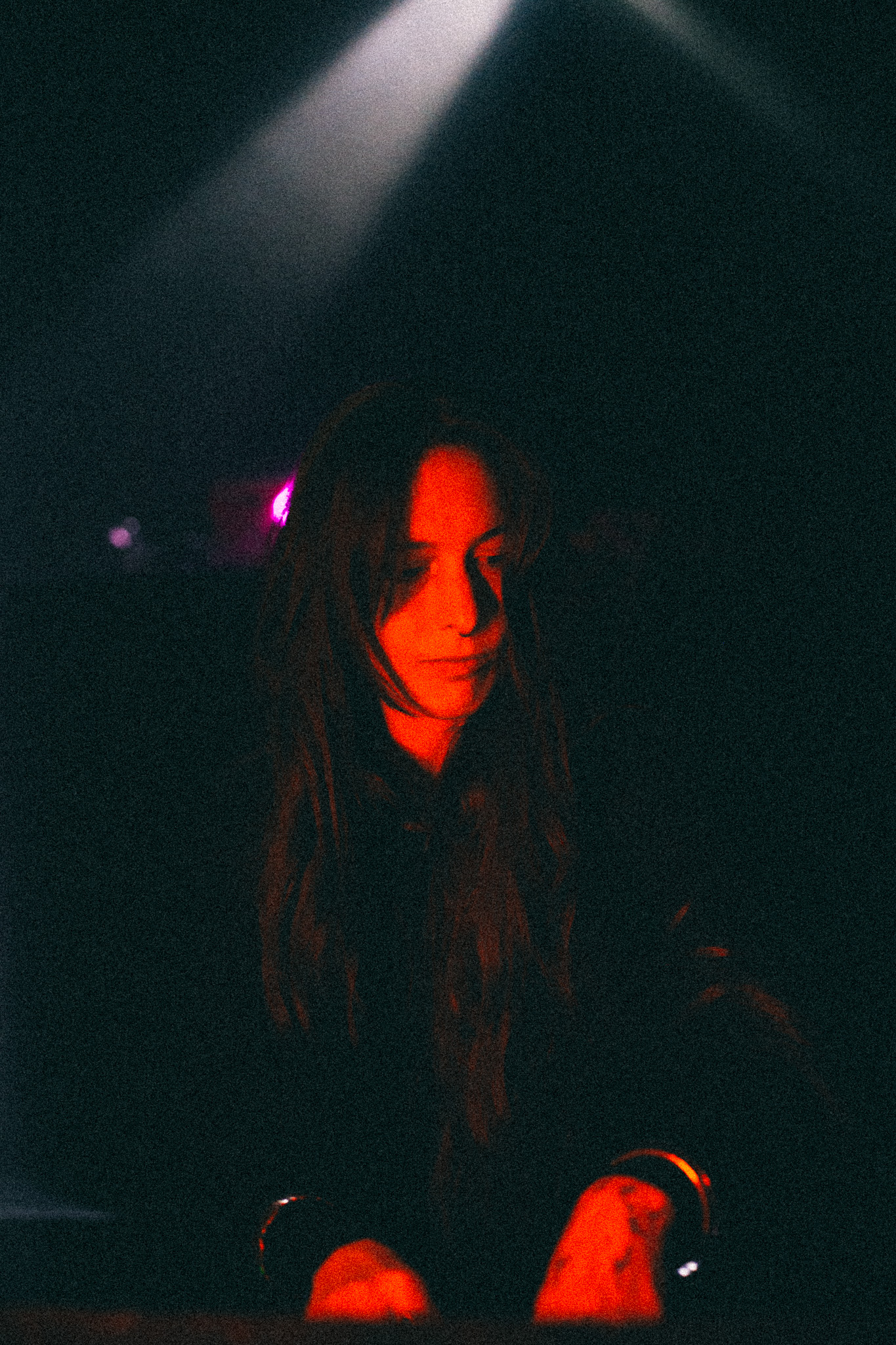 Close portrait of Ninon looking down at the decks, lit red from below