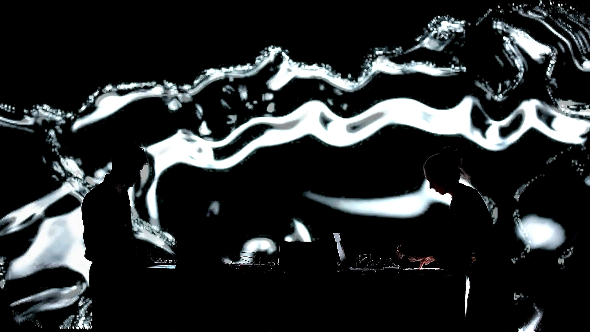 The duo in silhouette against a liquid, metallic generative image filling the wall behind them