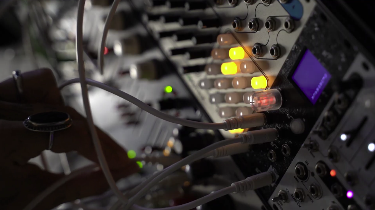 A hand patching a Eurorack case; the Neurorack module's amber indicator LEDs and small display are lit